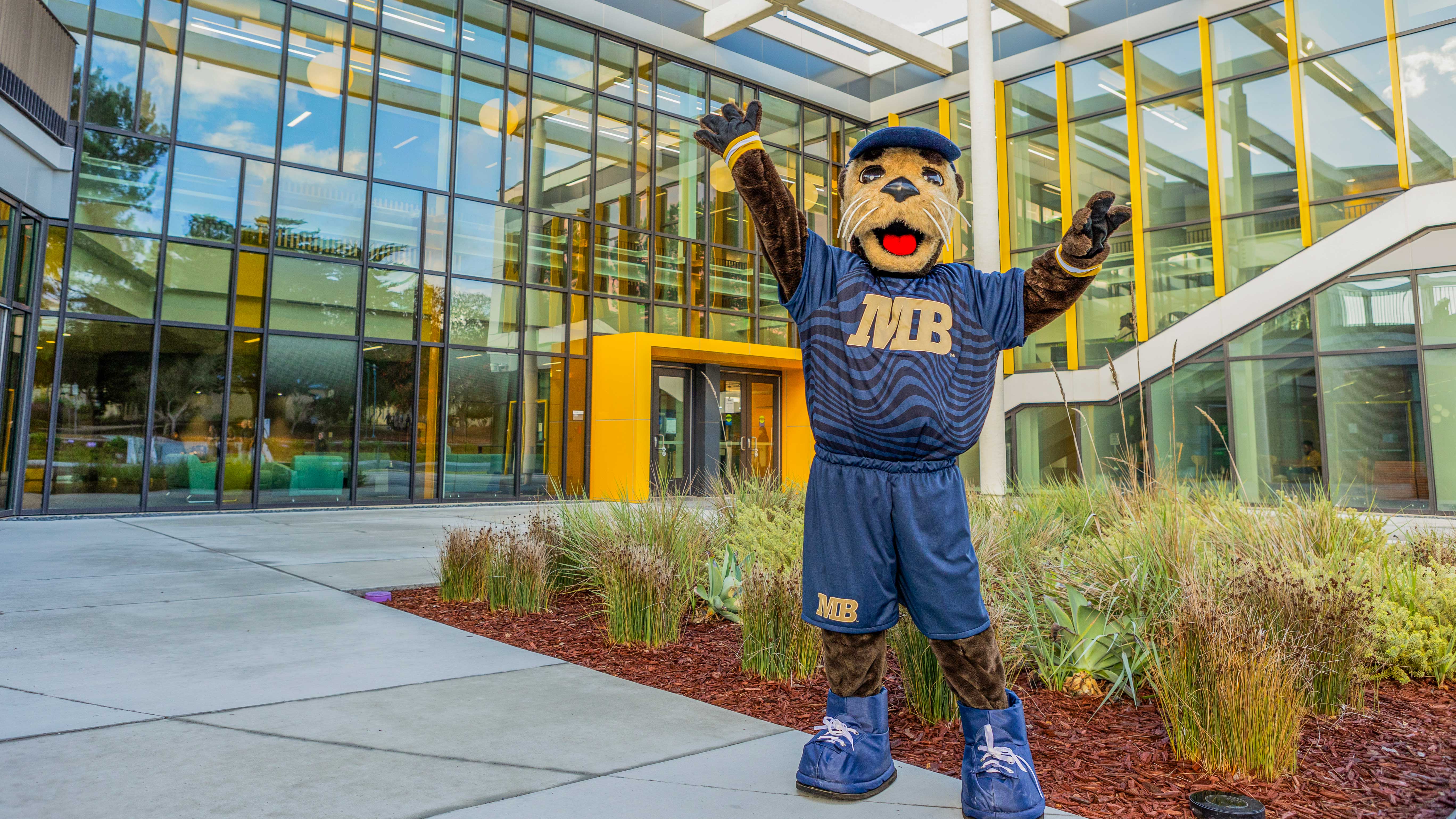 mascot posing with his arms up outside on campus