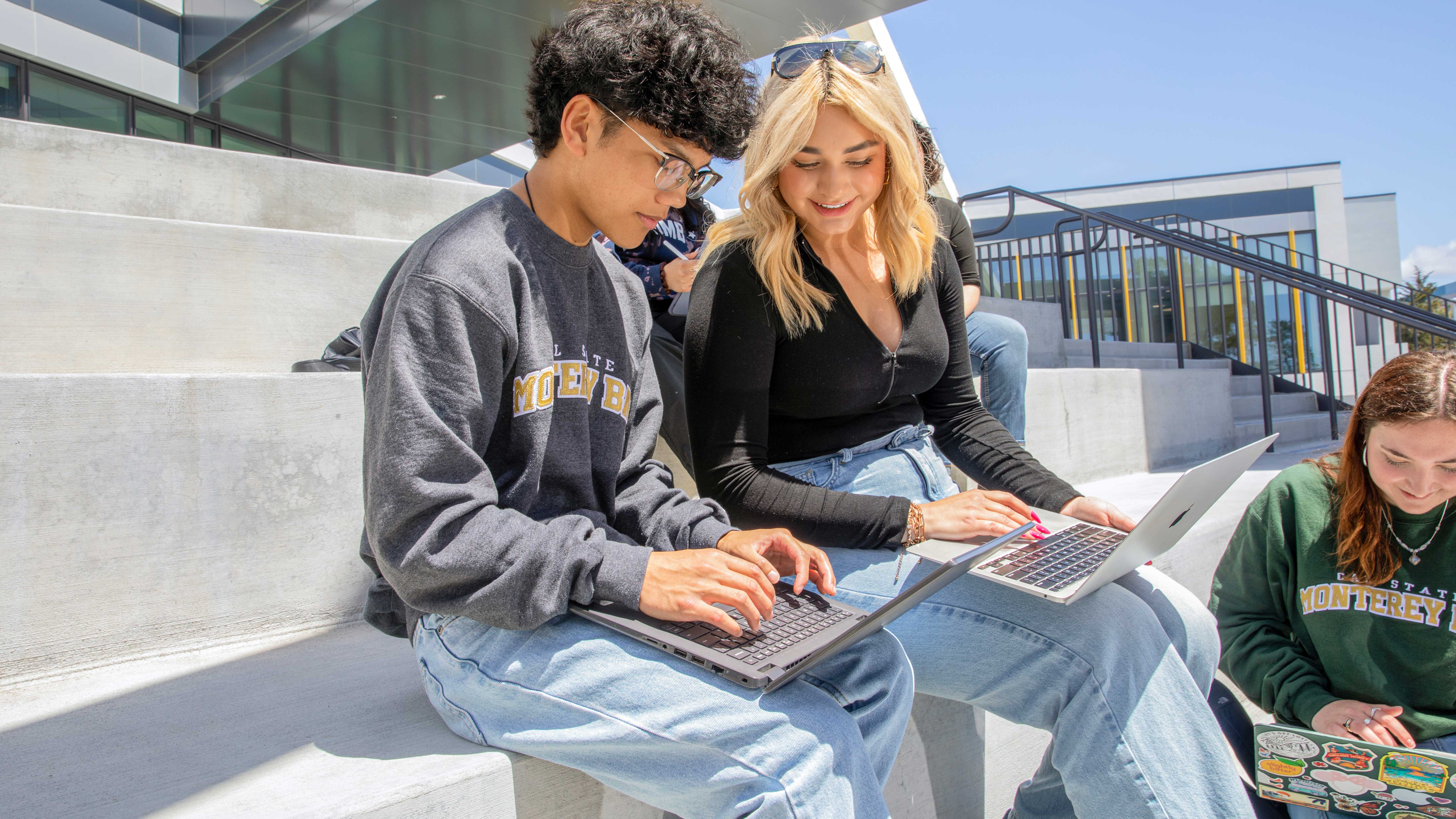 two students sitting outside on the steps working on their laptops