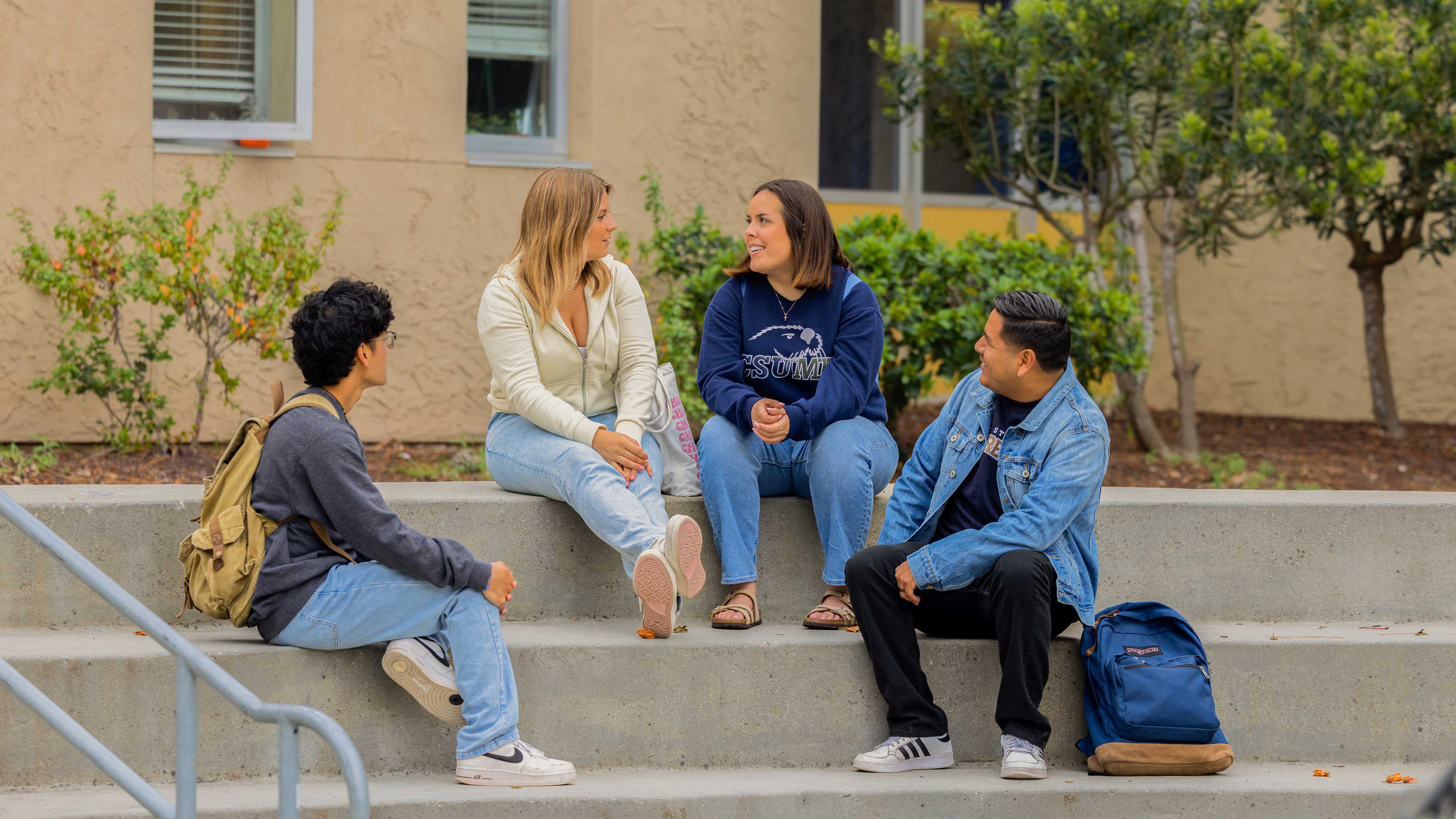 four students sitting on the steps outside on campus socializing